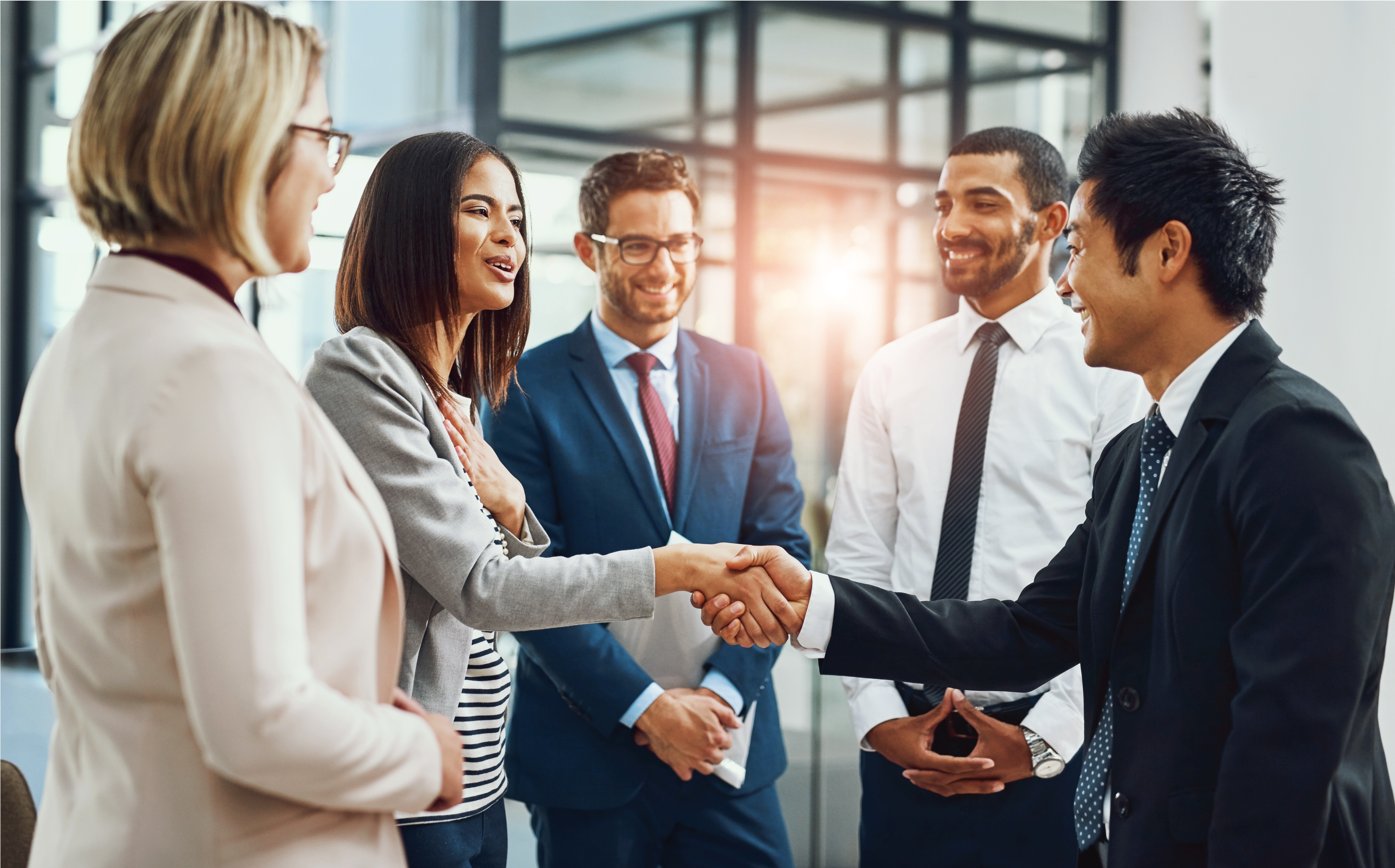 Group of professionals engaging in a handshake and conversation in an office setting.